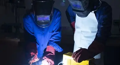 2 personnes adultes travaillant le métal sur un poste à souder. Les Inventeurs proposent des ateliers de soudure à l'arc.