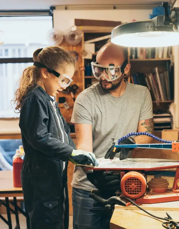 Un enfant utilise une scie à chantourner, aidé par un adulte