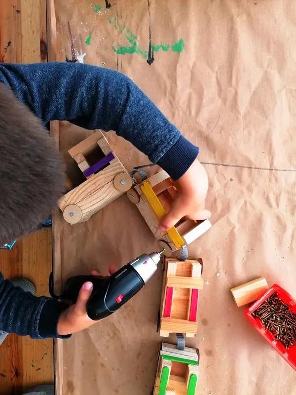 un enfant fabrique un train en bois, un enfant manipule une visseuse