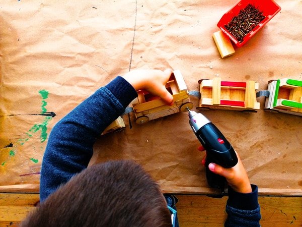 un enfant fabrique un train en bois, un enfant manipule une visseuse