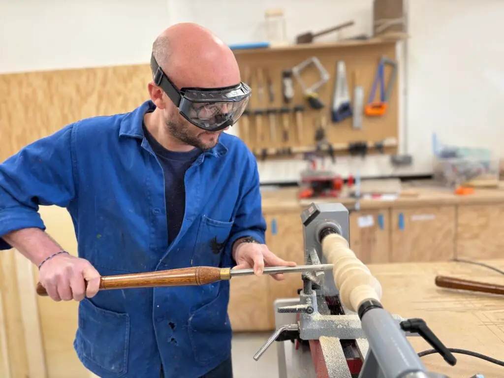 Formateur au tour à bois dans l'atelier Les Inventeurs, équipé de lunettes de protection
